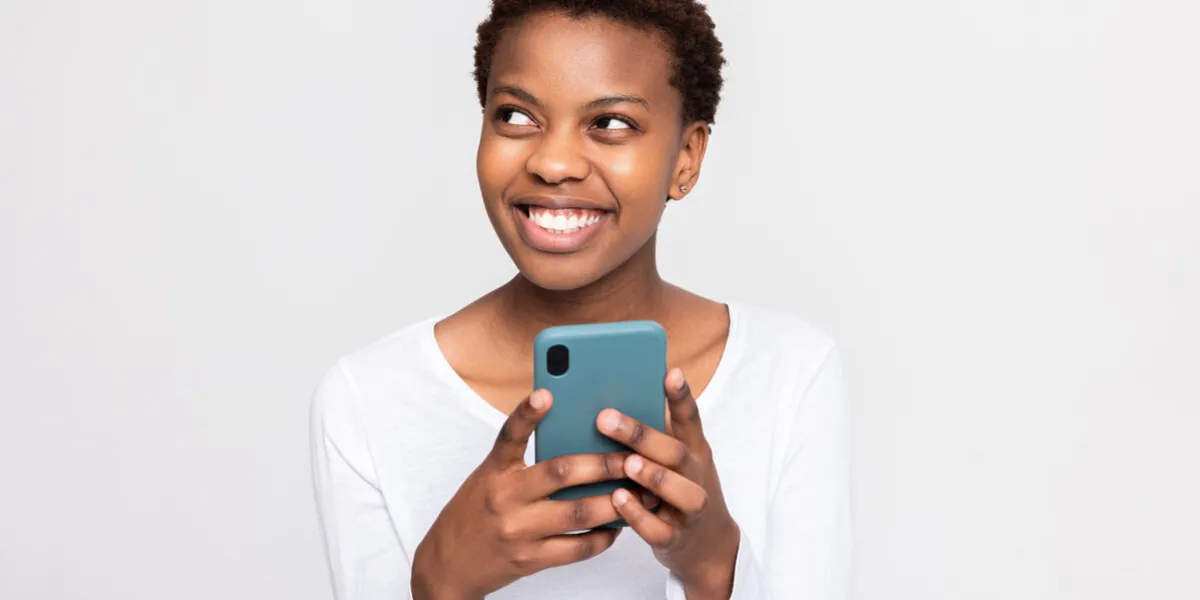 charming african woman with short haircut holding cellphone in hands chatting messaging with someone boyfriend friends family holding new modern device in arms