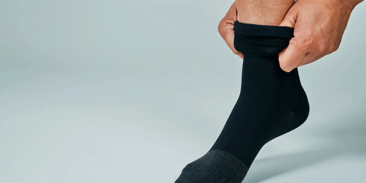 a man puts on a black compression sock in front of an off-white background with some blank space on the left