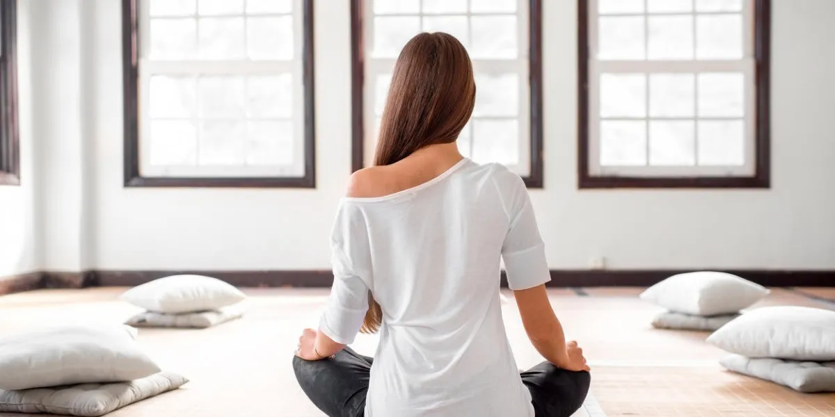 femme jeune et positive en t-shirt blanc et leggings noirs pratiquant le yoga dans l'intérieur lumineux avec de grandes fenêtres