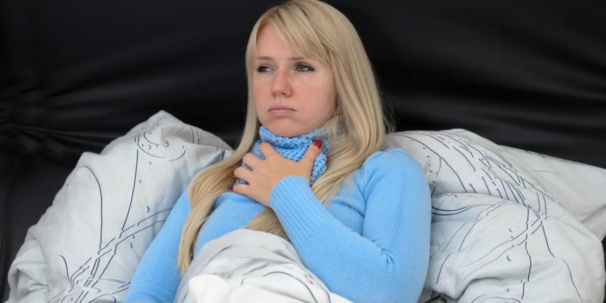 woman resting in bed propped up against the pillows suffering from a seasonal cold and flu clutching her chest and looking miserable