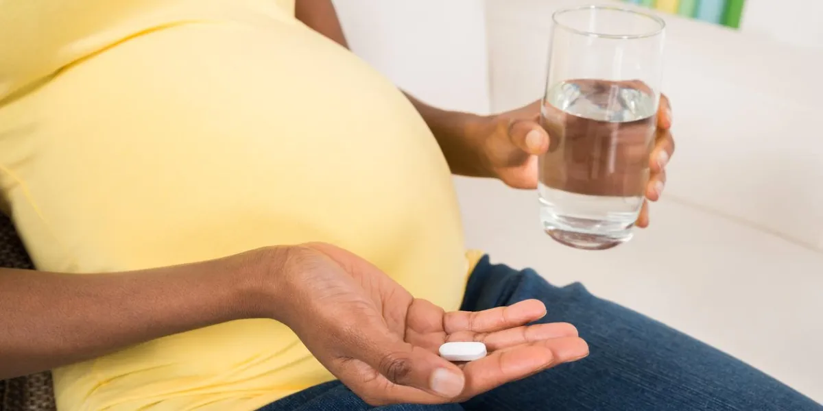 close-up of pregnant woman hand with glass of water and vitamin pill