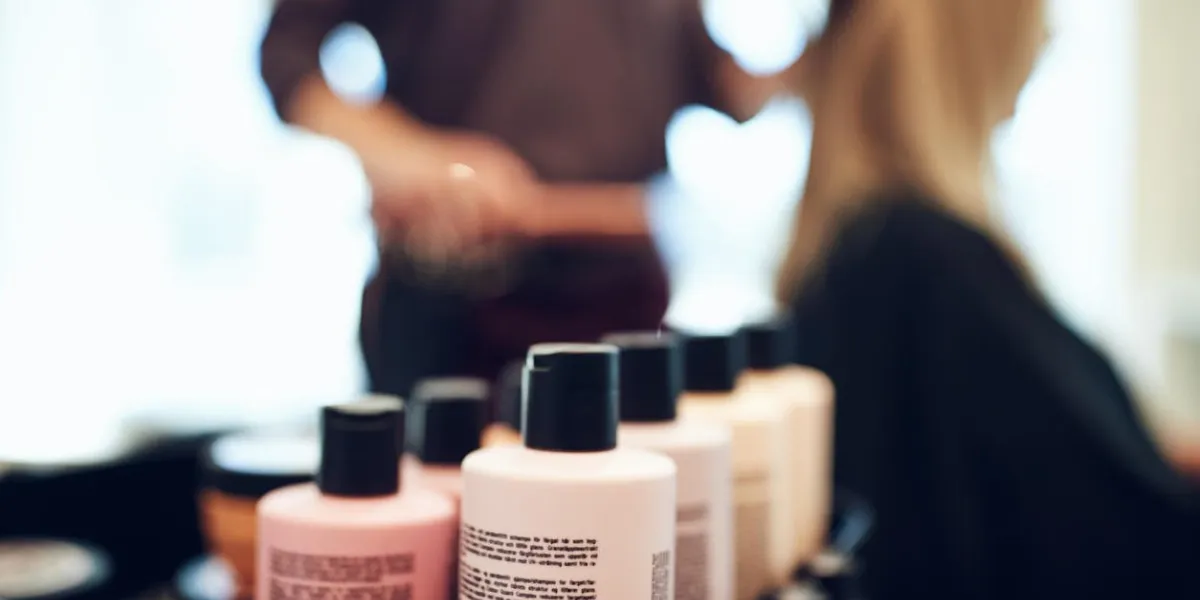 closeup of shampoo and conditioner bottles on a tray in a hair salon with a hairdresser styling a client's hair in the background