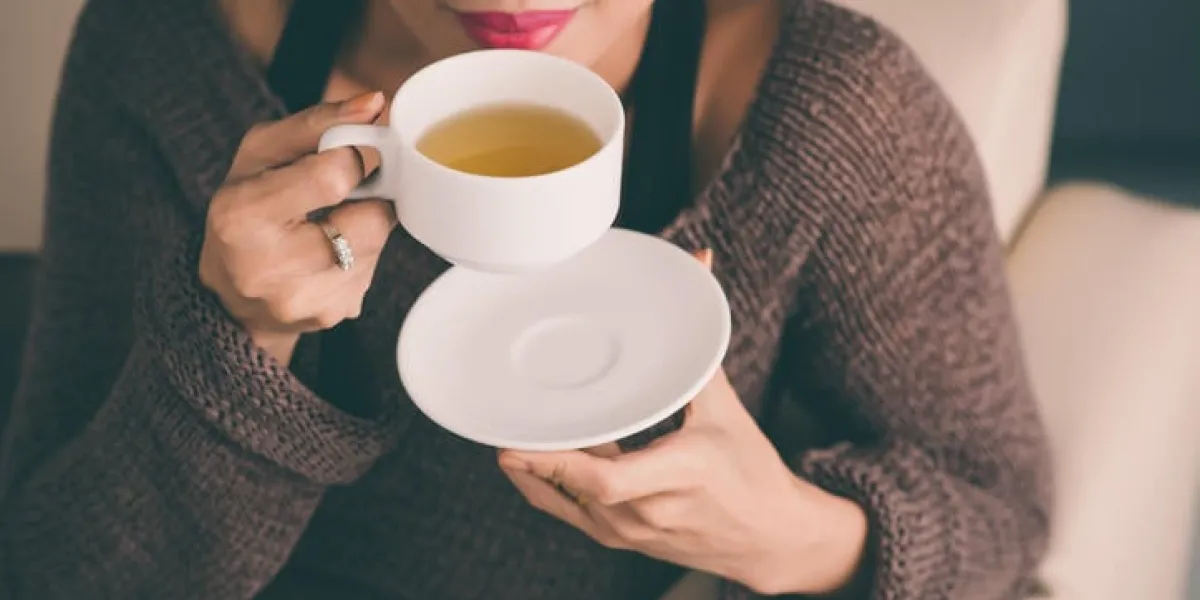 femme méconnaissable tenant une tasse de thé chaude et soufflant dessus