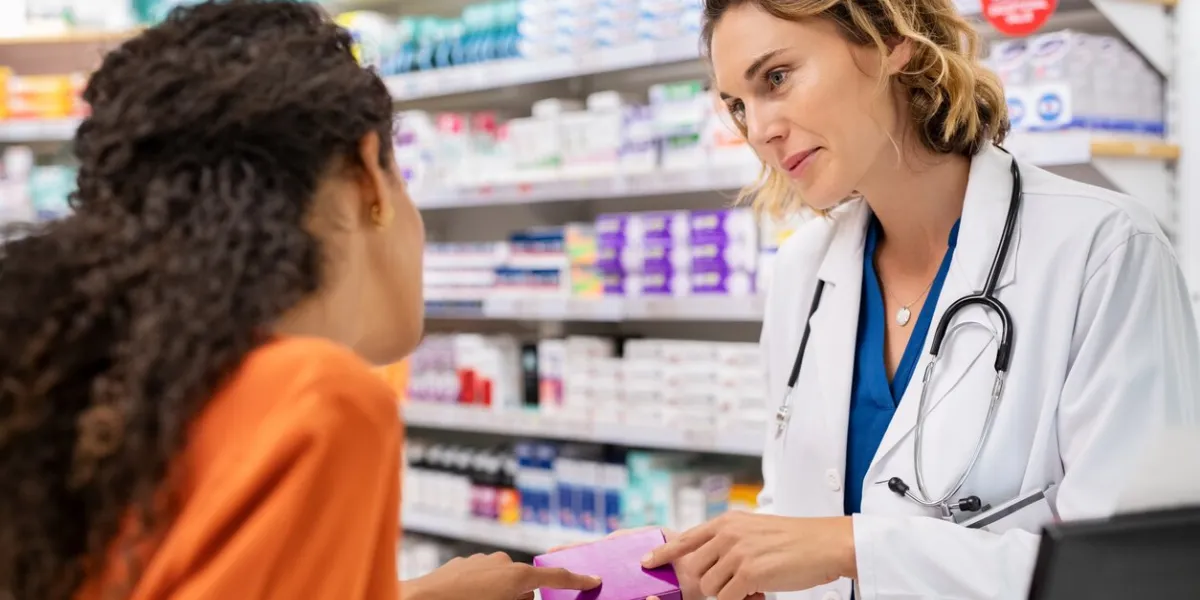 pharmacist giving medicine box to customer in pharmacy doctor showing and explaining medicine dose to customer mature pharmacist giving advice on medicaments, while serving young african woman