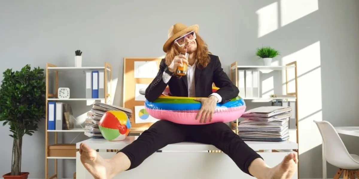 annual leave and planning travel vacation concept funny office worker waiting for summer holidays happy barefoot employee in sun hat, sunglasses and swim ring sitting on desk and drinking cocktail