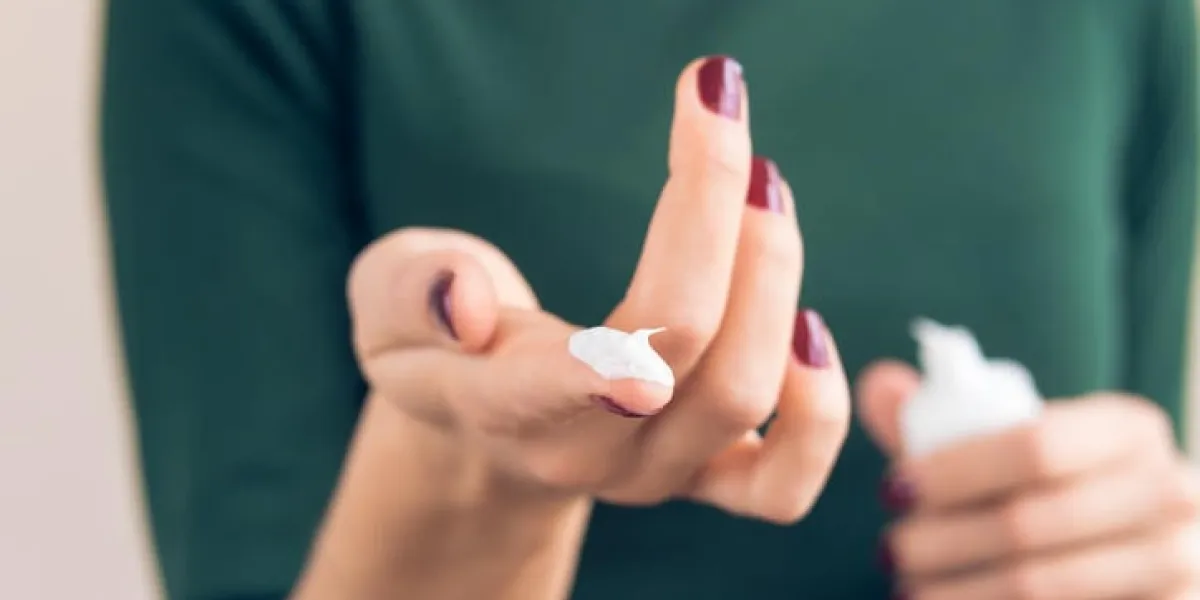 femme dans un t-shirt vert et une manucure marron montre la crème pour les mains sur le doigt