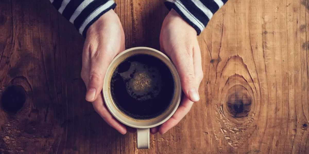 femme solitaire, boire du café le matin, vue de dessus des mains féminines tenant la tasse de boisson chaude sur le bureau en bois, rétro tonique