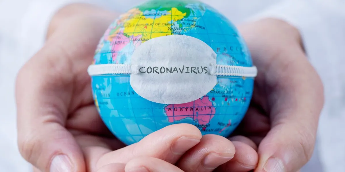 closeup of a caucasian doctor man holding a world globe with a protective mask with the word coronavirus written in it