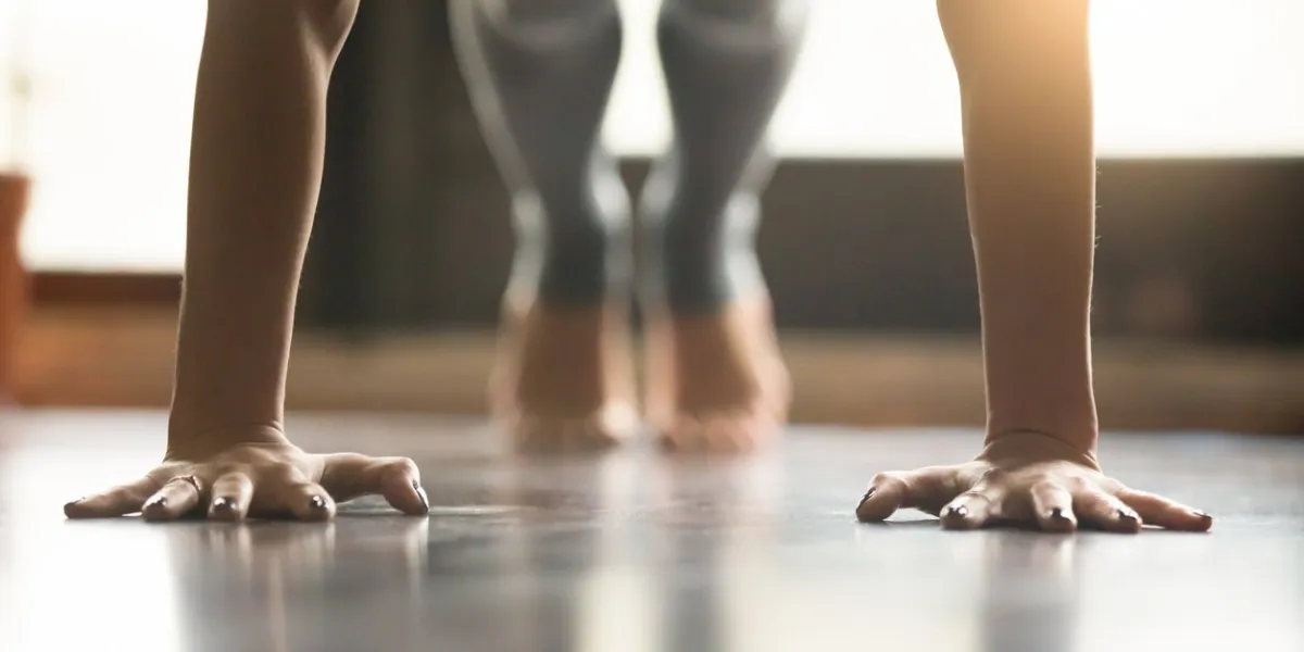 young woman practicing yoga, doing push ups or press ups exercise, phalankasana plank pose, working out, wearing sportswear, grey pants, indoor, home interior, living room floor close-up of hands