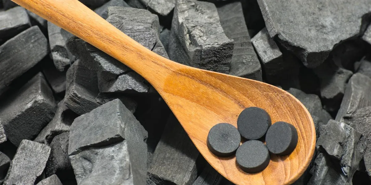 activated carbon pill in wood spoon on charcoal texture background