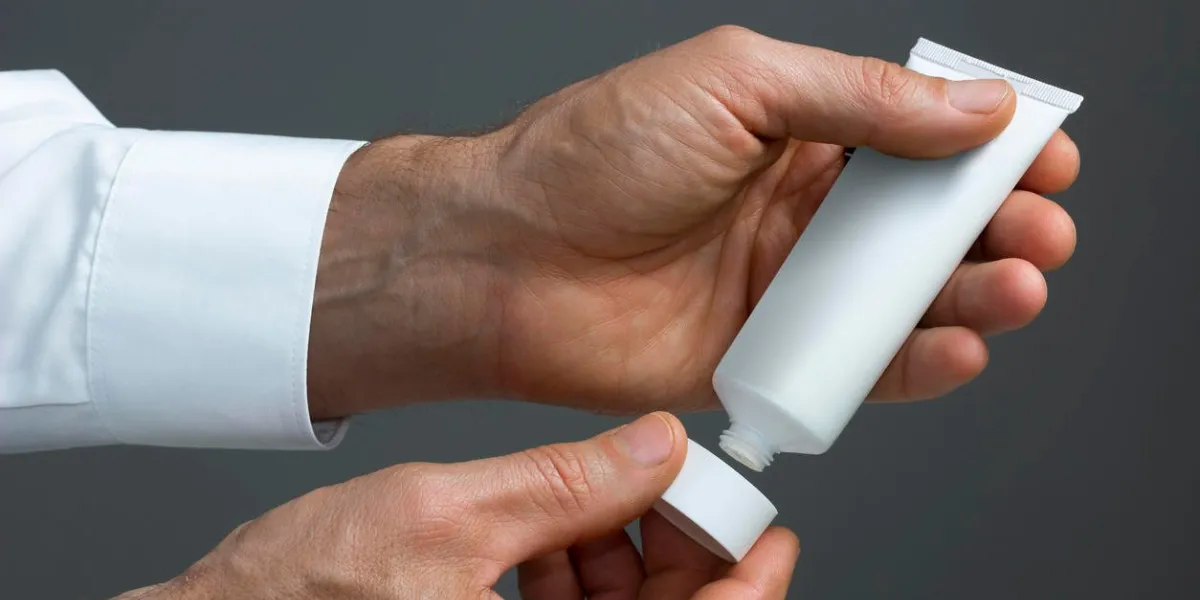 les mains de deux hommes avec un tube de crème blanche ouvert