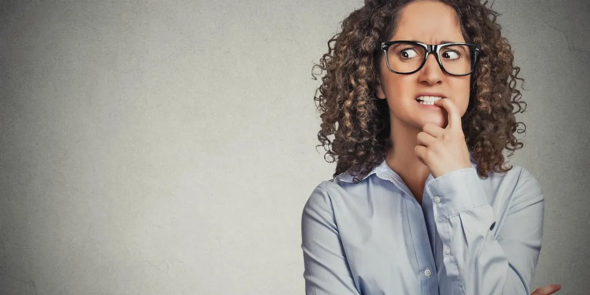 closeup portrait nervous woman with glasses biting her fingernails craving for something, anxious isolated grey wall background with copy space negative human emotion, facial expression body language