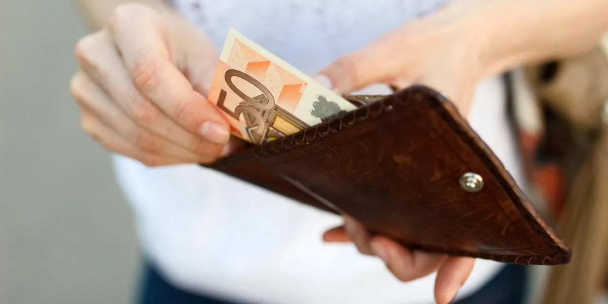 girl is taking out a banknote of fifty euros from brown leather wallet on the street hands, money and wallet close-up