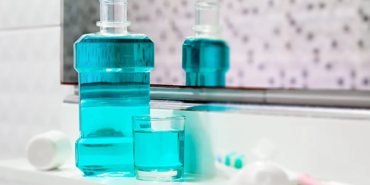 oral cleanser for good oral health, bottle and glass of mouthwash on bath shelf with blurred toothbrush and toothpaste in foreground
