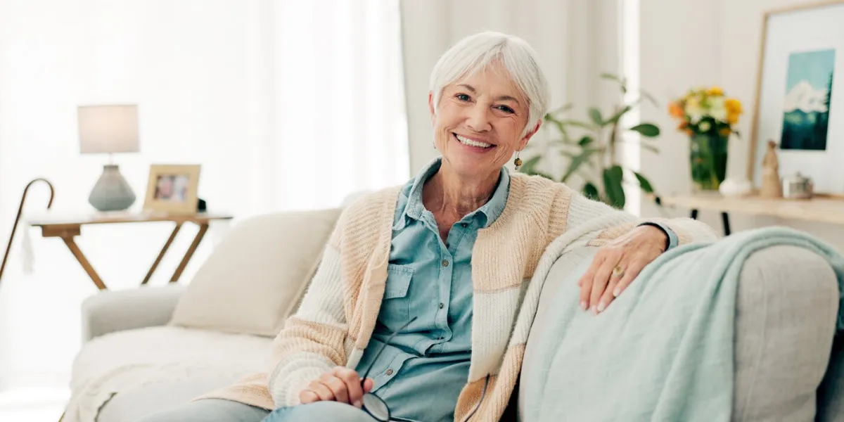 happy, senior woman and relax on sofa in nursing home or grandma with happiness, freedom and retirement in house portrait, elderly person and smile in living room or thinking of good memory