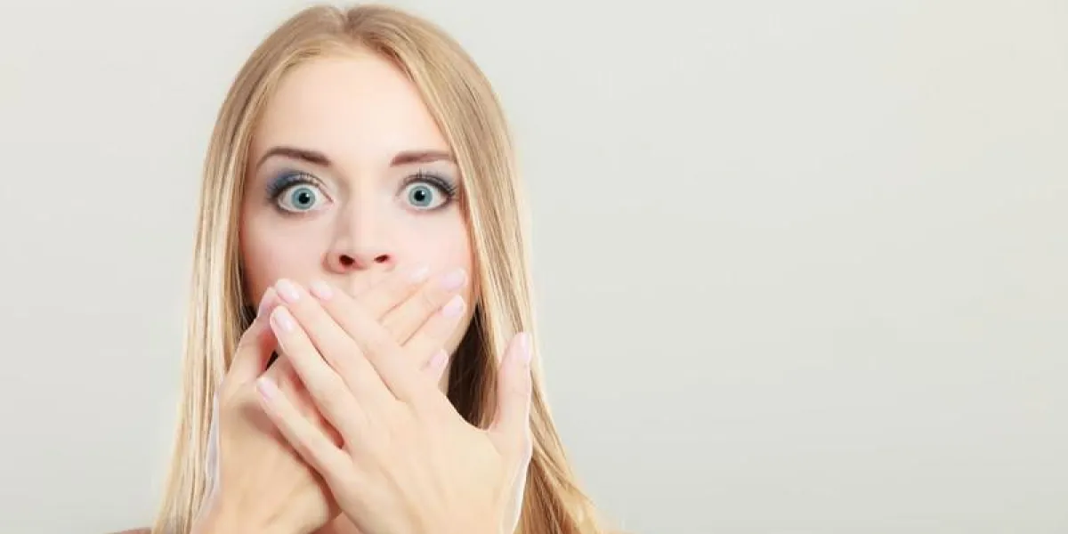 closeup jeune étonné femme large yeux couvrant sa bouche avec les mains sur gris
