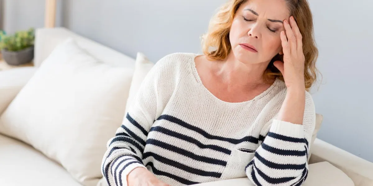 femme mature souffre de maux de tête, elle est assise sur le canapé et toucher le temple ses yeux sont fermés de frustration