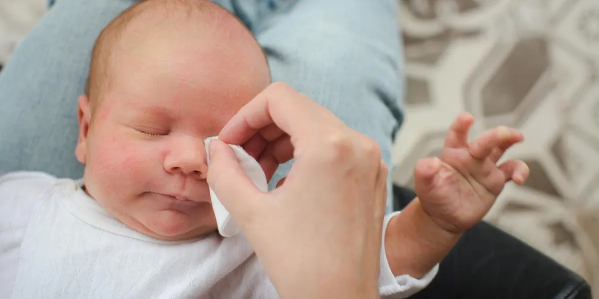mother cleaning eyes of a newborn baby with physiological solution on a cotton strip, top view