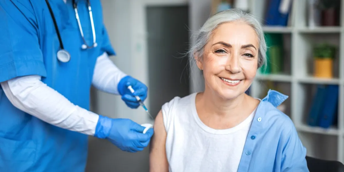 millennial man doctor make injection to smiling elderly lady patient in clinic office interior treatment, medical health care, vaccination and immunization of retired during flu and covid-19 outbreak