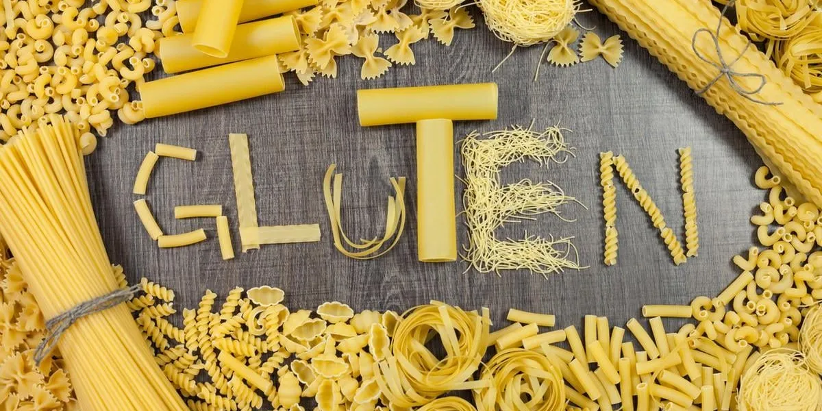 various pasta shapes with gluten word on a wooden surface