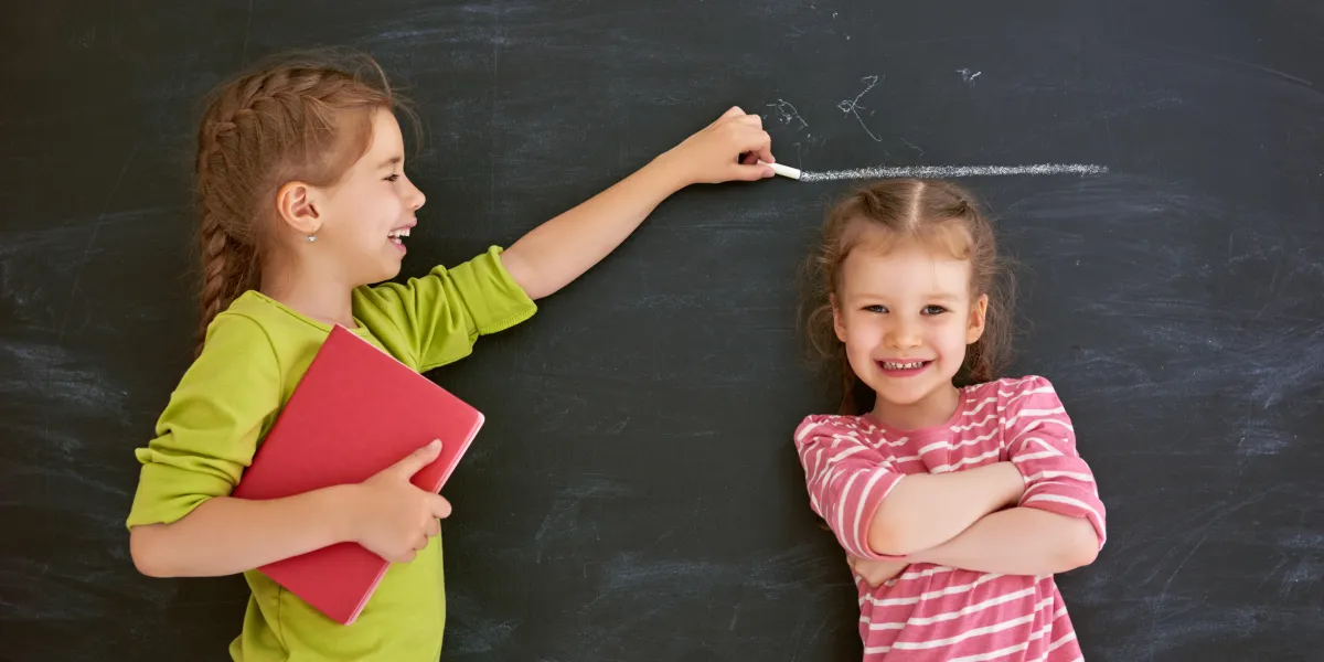 two children sisters play together kid measures the growth on the background of blackboard concept of education