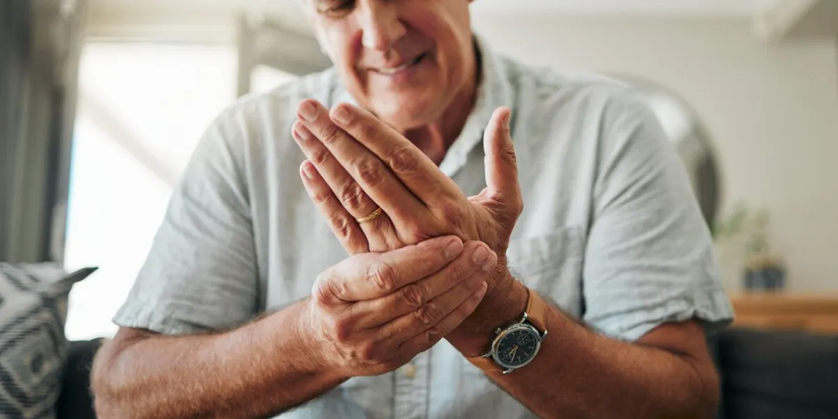 hands, pain and arthritis with a senior man holding his hand while suffering from osteoporosis, cramp or injury health, medical and joint with an elderly male pensioner in the living room at home