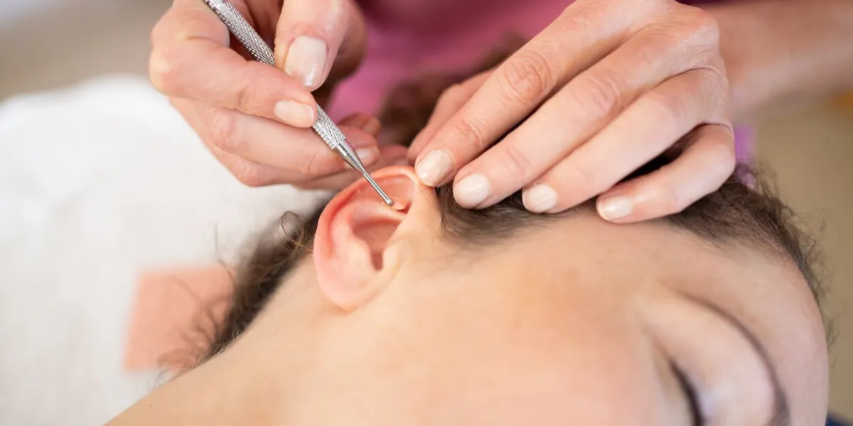 crop professional chiropractor applying auriculotherapy ear acupuncture techniques on female client lying in modern beauty salon during skin care treatment