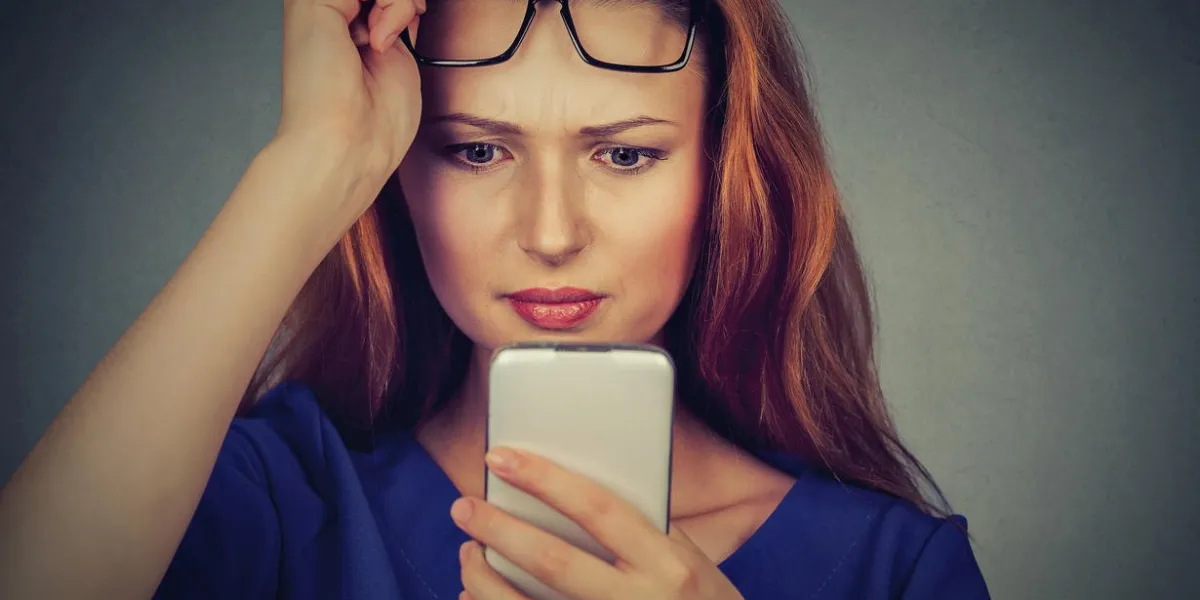 closeup portrait headshot young woman with glasses having trouble seeing cell phone has vision problems bad text message negative human emotion facial expression perception confusing technology