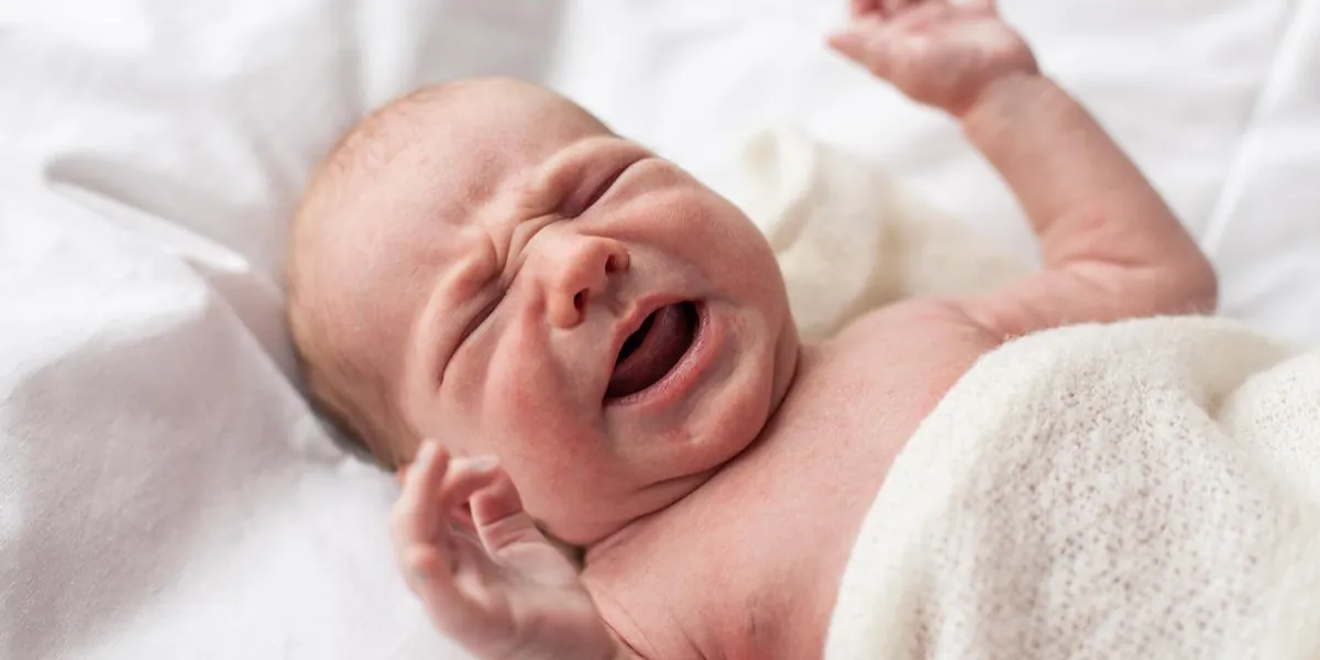 closeup of newborn baby crying lying down on bed