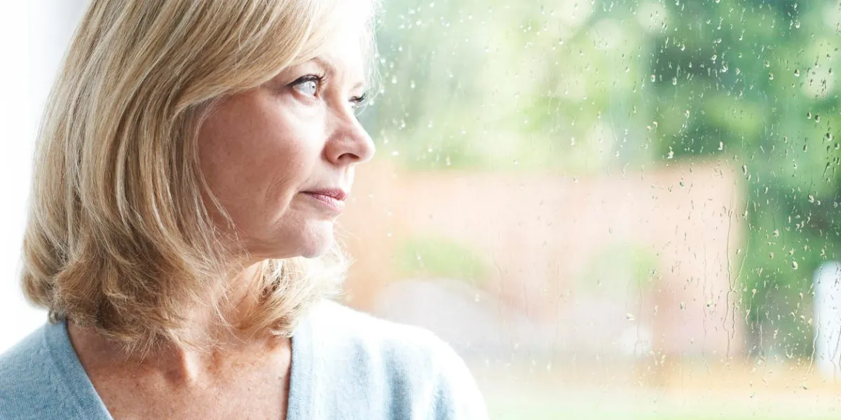 sad mature woman suffering from agoraphobia looking out of window