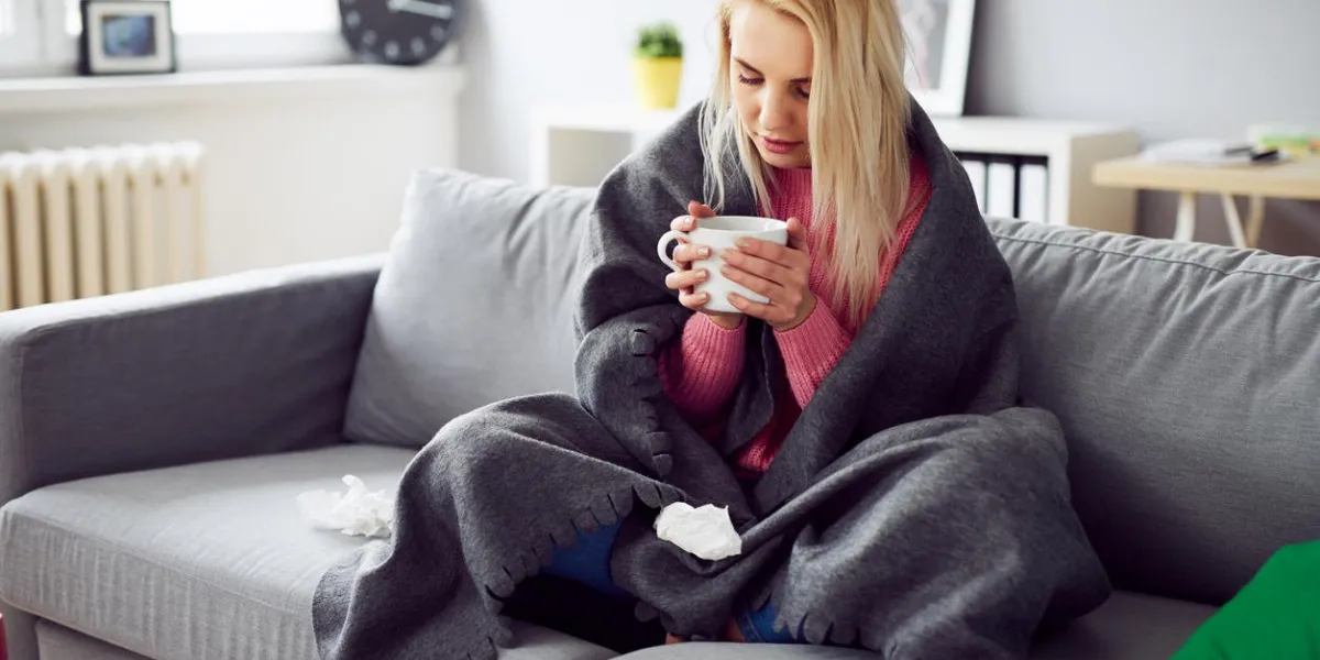 young woman drinking tea while covered in blanket