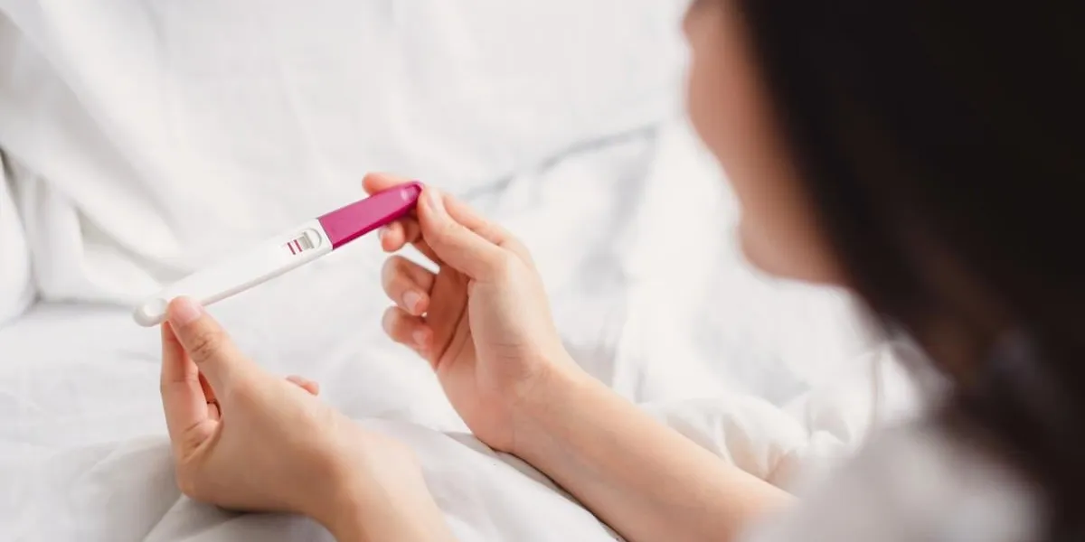 back view of happy smile woman looking at pregnancy test with positive result in hand on the bed