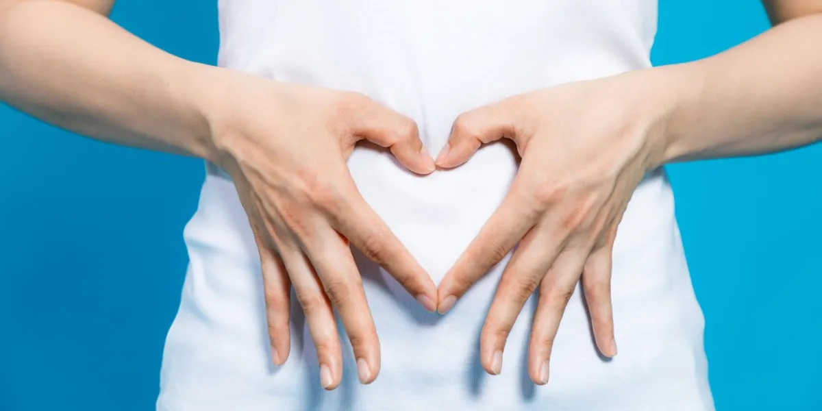 young woman who makes a heart shape by hands on her stomach