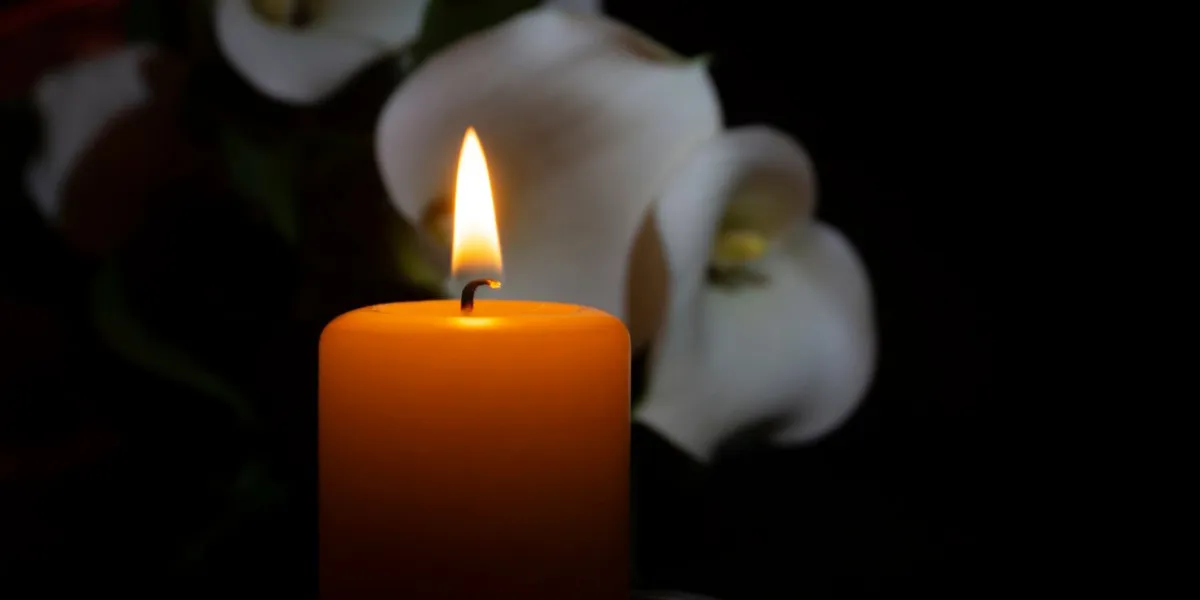a close up of an orange candle and flame and lily flowers on a dark background