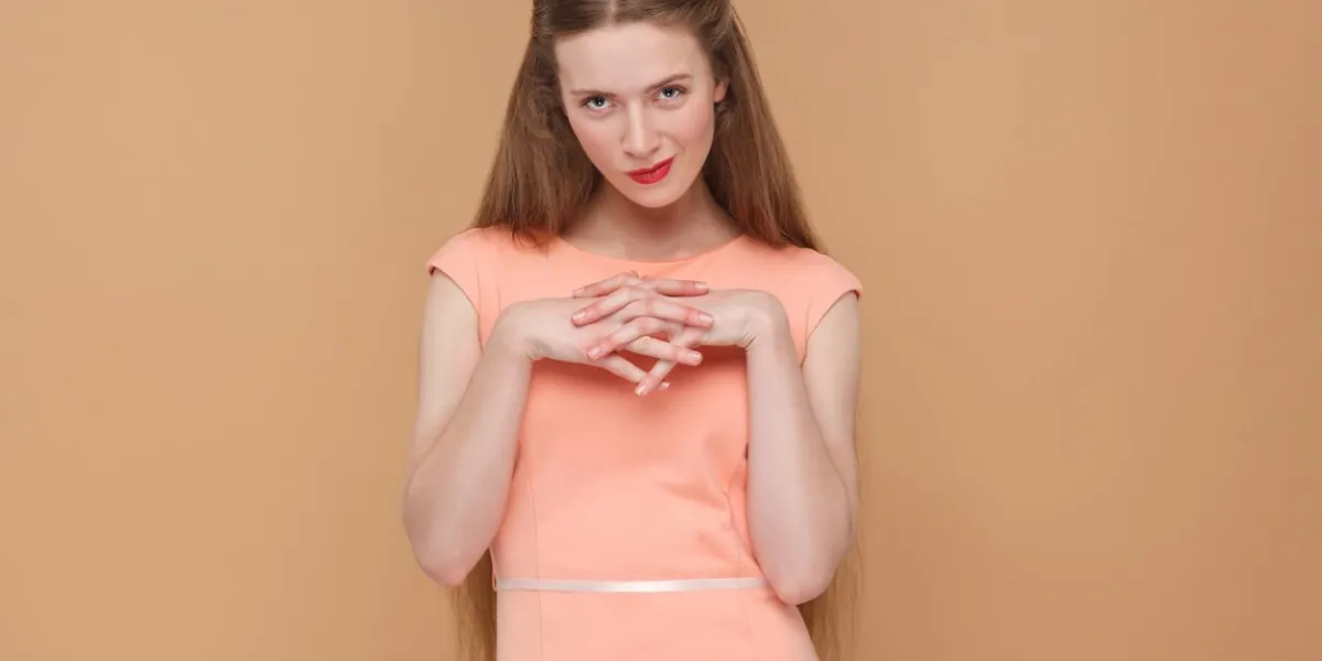 cunning plan, looking at camera portrait of emotional cute, beautiful woman with makeup and long hair in pink dress indoor, studio shot, isolated on light brown or beige background