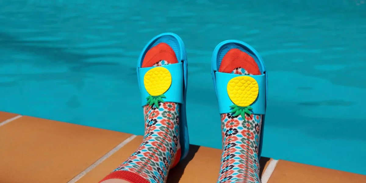 feet with colorful socks and blue pool sandals at the edge of a swimming pool summer concept aesthetic summer