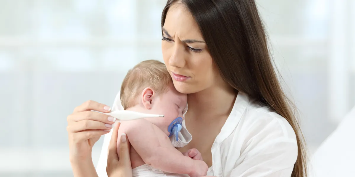 mother checking thermometer holding her ill baby at home