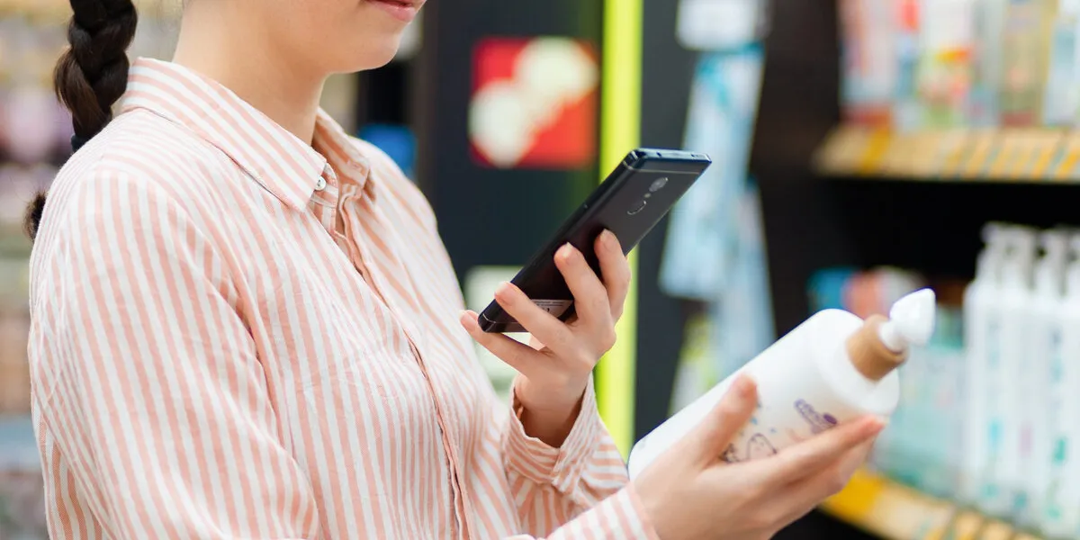 close up of woman holds smartphone and scanning qr code on bottle of cosmetics concept of modern shopping