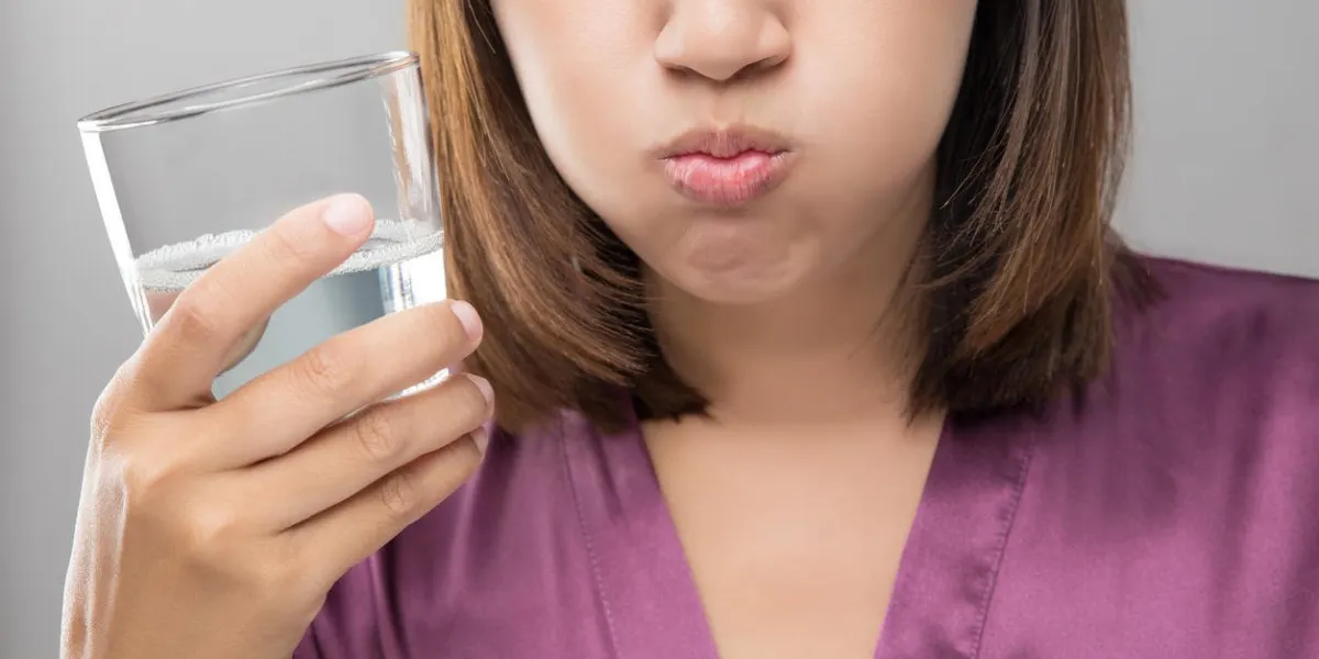 femme se rincer et se gargariser en utilisant un rince-bouche à partir d'un verre, au cours de la routine quotidienne d'hygiène buccale, fille dans une robe de soie violette, les concepts de soins dentaires