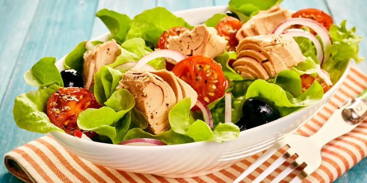 delicious healthy fresh tuna salad served outdoors on a wooden table with leafy greens, tomato, olive and onion