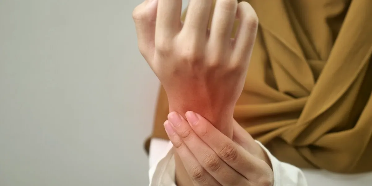 anonymous woman touching her wrist, suffering from arthritis disease, close up against grey background