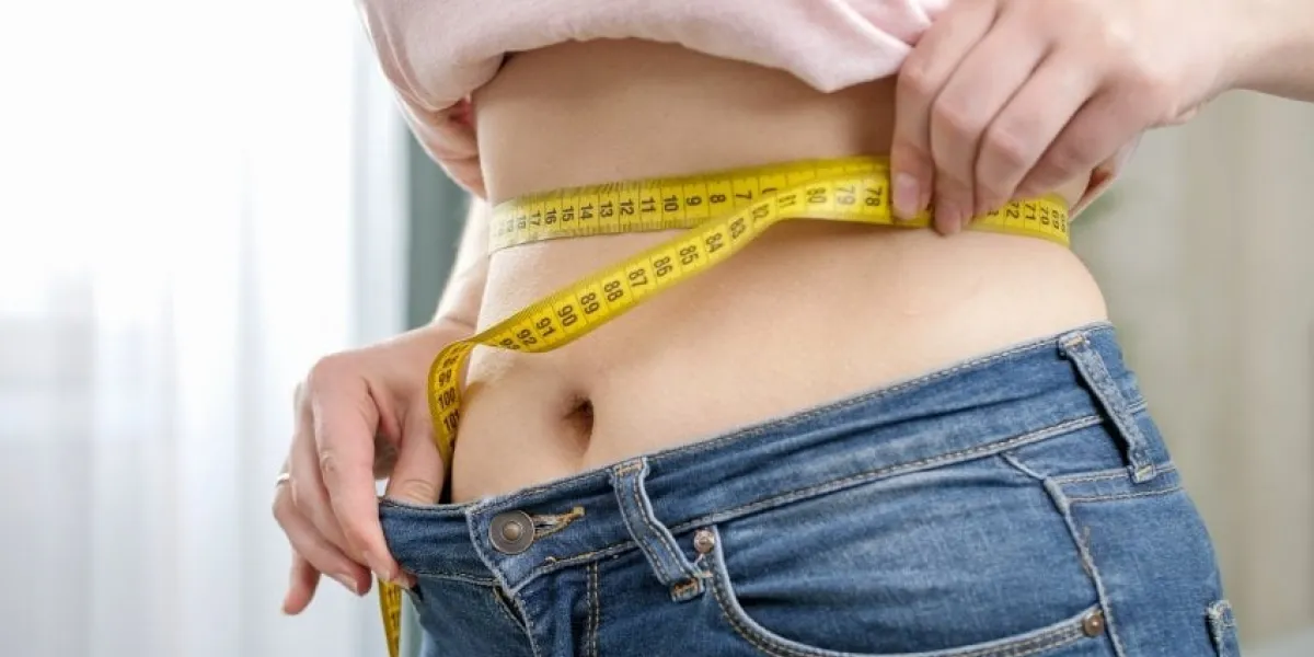 closeup of young woman with slim belly measuring her waist at mirror in bedroom concept of dieting, loosing weight and healthy lifestyle