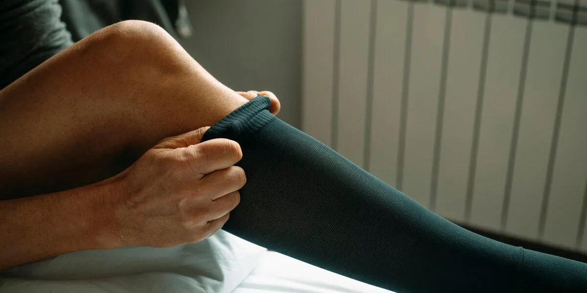 closeup of a man putting on a compression sock sitting on the bed at home