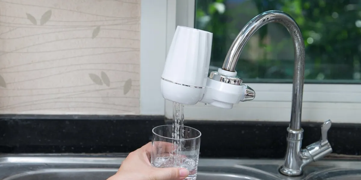 woman pouring water into glass from the water filter in the kitchen pouring clean fresh drink