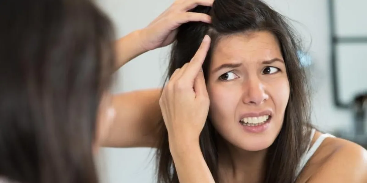 une jeune femme horrifiée qui regarde dans le miroir de la salle de bain, la bouche ouverte, regarde les premiers cheveux gris sur son cuir chevelu, un premier signe de vieillissement, ou remarque qu'elle souffre de pellicules