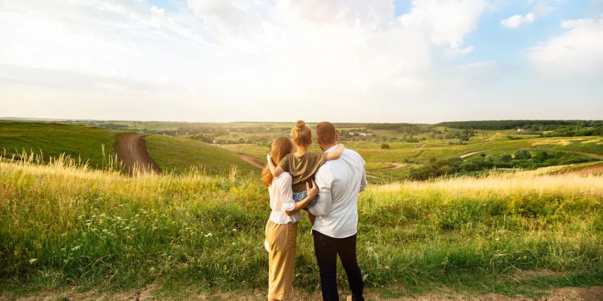 happy family concept back view of mother, father and daughter looking and enjoying landscape on sunset