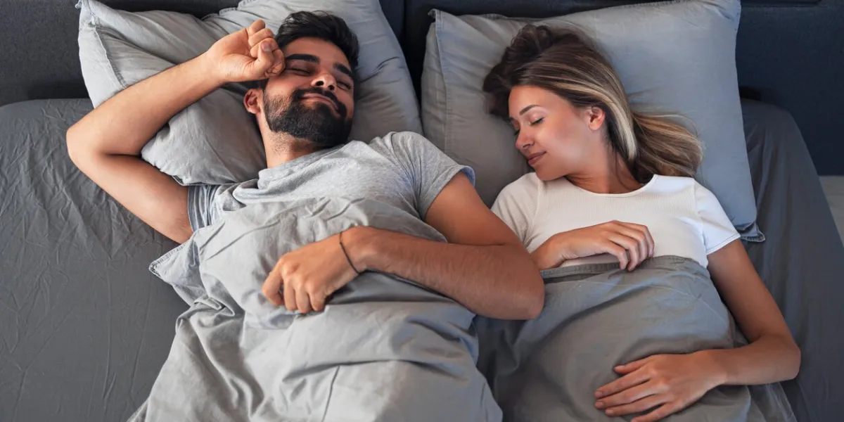 happy young couple sleeping on cozy bed and smiling handsome man is waking up