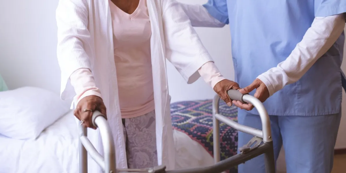 mid section of mixed race female nurse helping senior mixed race female patient to stand with walker