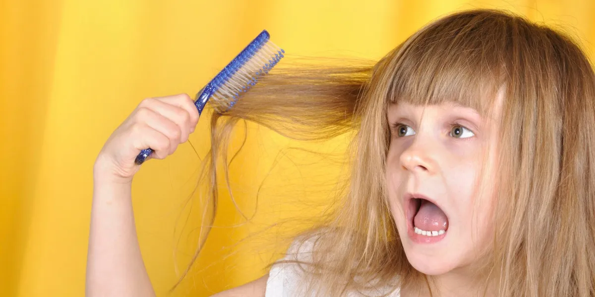 petite fille essayant de se brosser les cheveux avec une brosse à cheveux