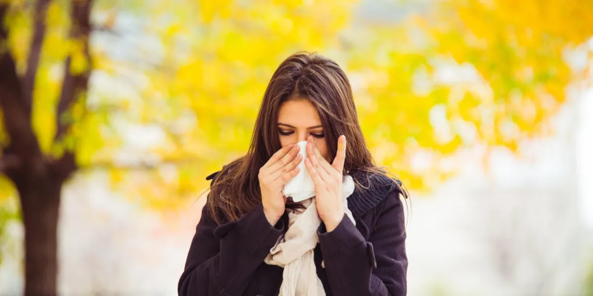 young girl in autumn park blowing nose standing in park in warm clothing holding tissue